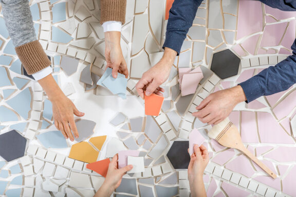 Three peoples hands working for mosaic work on a table.