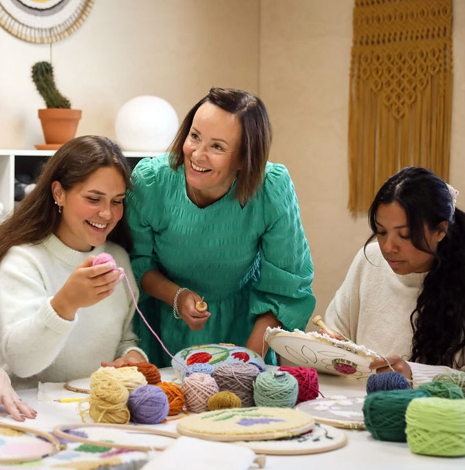 Three women making punch needle crafts beside a table.