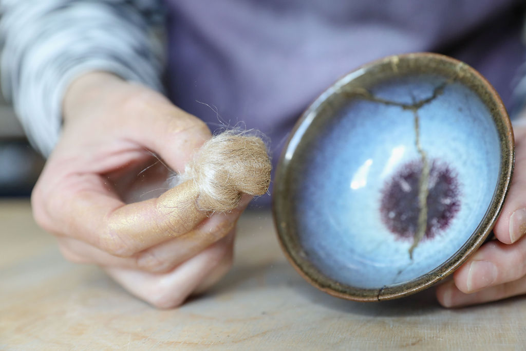 Silkkikuitupallerolla töpötetään kultajauhetta astian kintsugi korjaussaumaan .